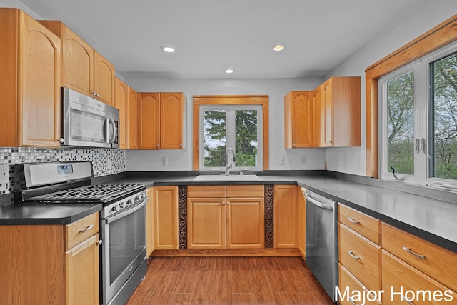 kitchen featuring dark countertops, appliances with stainless steel finishes, a sink, recessed lighting, and wood finished floors