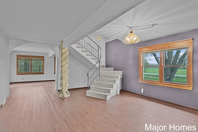 interior space featuring arched walkways, wood finished floors, baseboards, a chandelier, and stairs