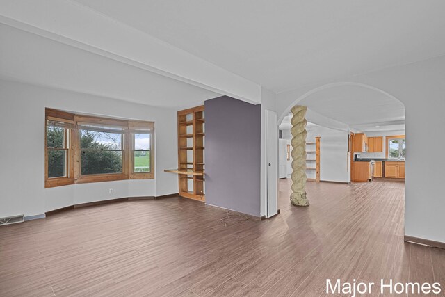 unfurnished living room featuring visible vents, arched walkways, wood finished floors, baseboards, and ornate columns