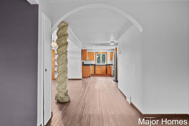 corridor featuring arched walkways, baseboards, visible vents, and light wood-type flooring