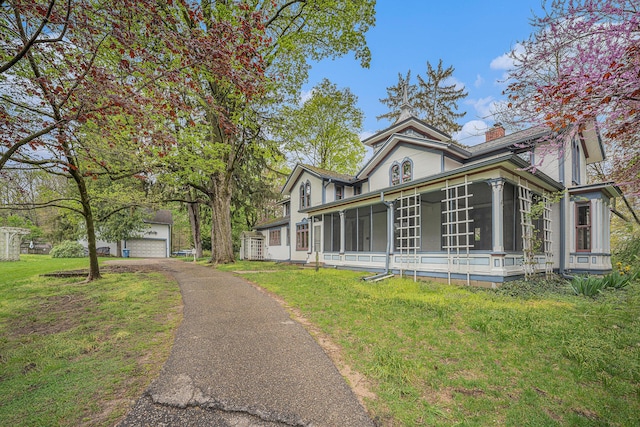 view of front of home featuring a garage, a front yard, a chimney, a sunroom, and an outbuilding