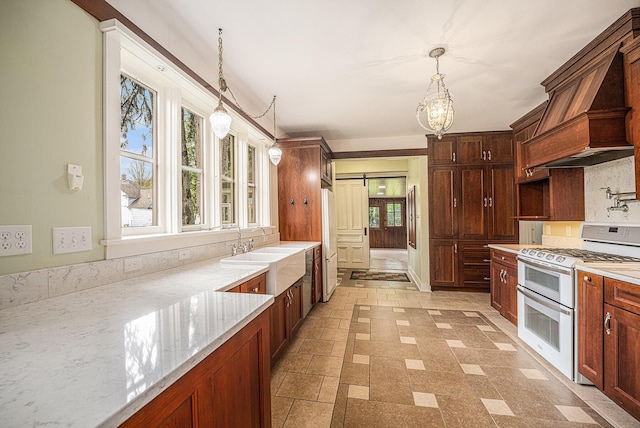 kitchen with hanging light fixtures, light stone countertops, a sink, custom range hood, and white appliances