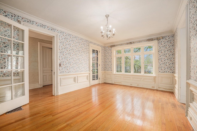 empty room featuring light wood-style floors, a chandelier, wallpapered walls, visible vents, and ornamental molding