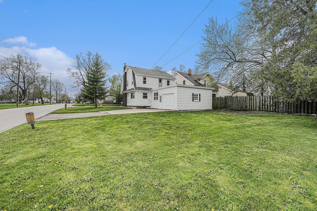 view of side of home with a garage, fence, a chimney, concrete driveway, and a lawn