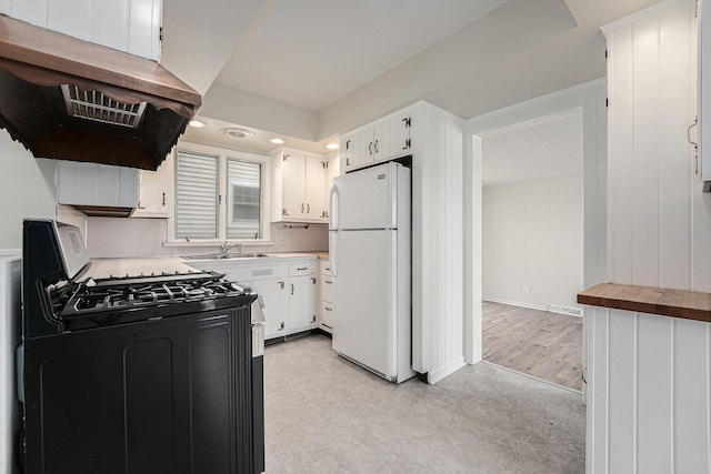 kitchen with freestanding refrigerator, white cabinetry, under cabinet range hood, a sink, and gas stove