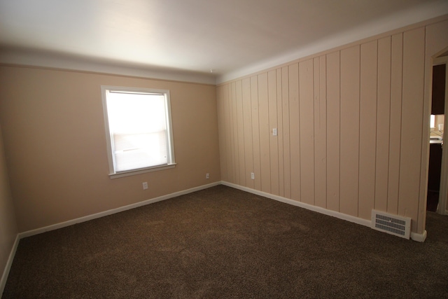 empty room with baseboards, dark colored carpet, and visible vents