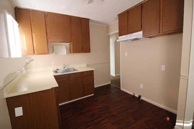 kitchen with a sink, light countertops, brown cabinetry, and under cabinet range hood