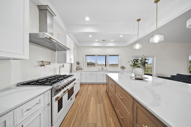 kitchen featuring wall chimney range hood, a sink, light wood finished floors, white cabinetry, and double oven range