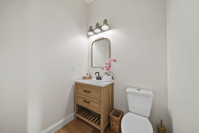 half bath with vanity, baseboards, wood finished floors, and toilet