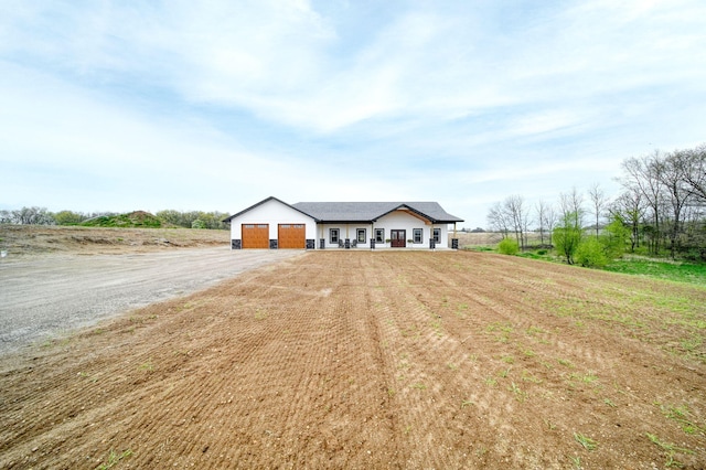 ranch-style home featuring dirt driveway, an attached garage, and a rural view