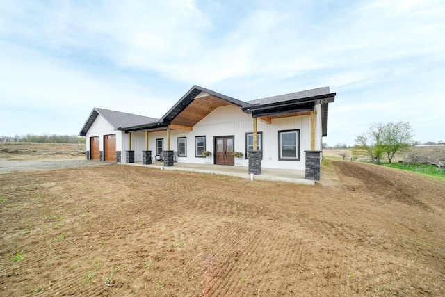 back of house with an attached garage, french doors, and dirt driveway