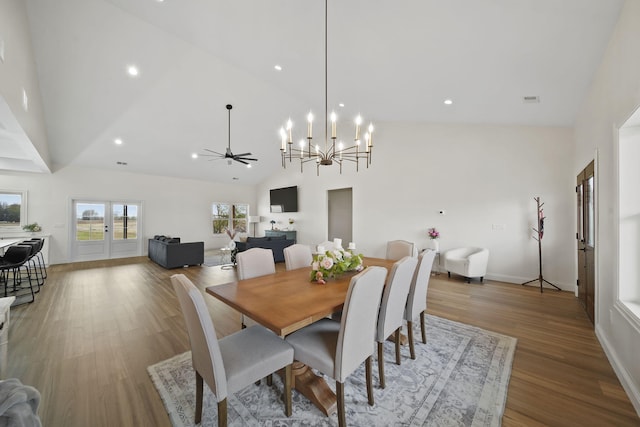 dining area with high vaulted ceiling, ceiling fan with notable chandelier, baseboards, wood finished floors, and visible vents