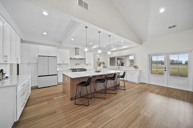 kitchen with light wood-style floors, white refrigerator, wall chimney exhaust hood, and visible vents