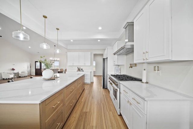 kitchen with wall chimney range hood, light stone countertops, light wood-style flooring, freestanding refrigerator, and range with gas cooktop