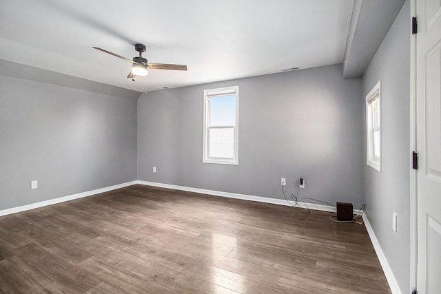 empty room with baseboards, visible vents, a ceiling fan, and dark wood-type flooring