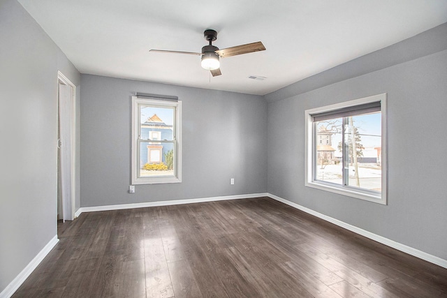 spare room featuring a healthy amount of sunlight, baseboards, a ceiling fan, and dark wood-type flooring