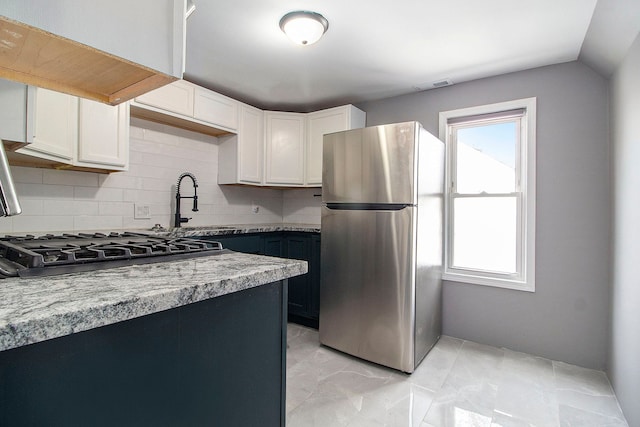 kitchen with backsplash, visible vents, a sink, white cabinets, and freestanding refrigerator