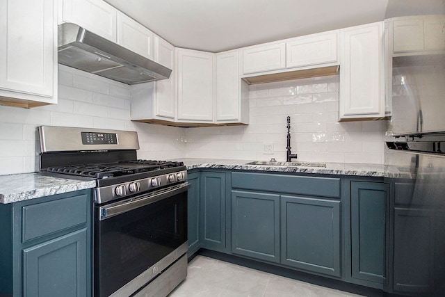 kitchen with wall chimney range hood, backsplash, blue cabinetry, a sink, and stainless steel gas range