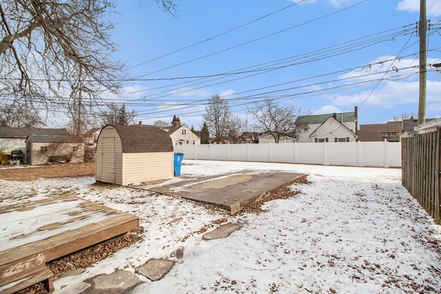yard layered in snow featuring a storage unit, a fenced backyard, and an outdoor structure