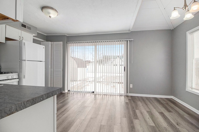 kitchen with a healthy amount of sunlight, dark countertops, white appliances, and light wood-style flooring