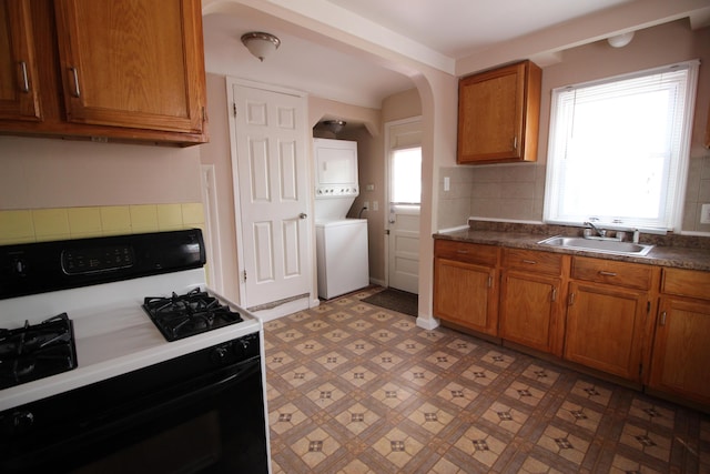 24648 Wilmot Ave, Eastpointe, MI 48021 - kitchen with stacked washer / drying machine, a sink, gas range, brown cabinetry, and tasteful backsplash