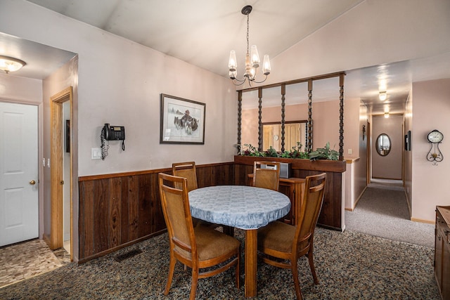 dining area with a chandelier, a wainscoted wall, and vaulted ceiling
