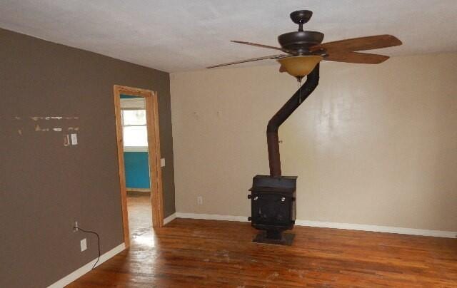 unfurnished living room featuring baseboards, a ceiling fan, a wood stove, and wood finished floors
