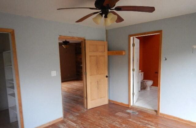 unfurnished bedroom with ceiling fan, baseboards, ensuite bathroom, and wood finished floors