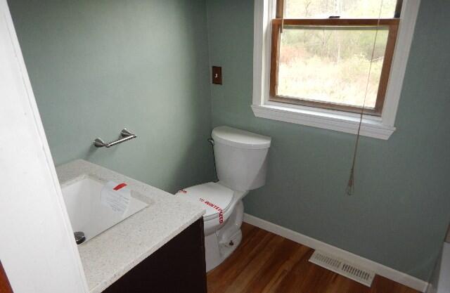 half bath featuring vanity, toilet, baseboards, wood finished floors, and visible vents