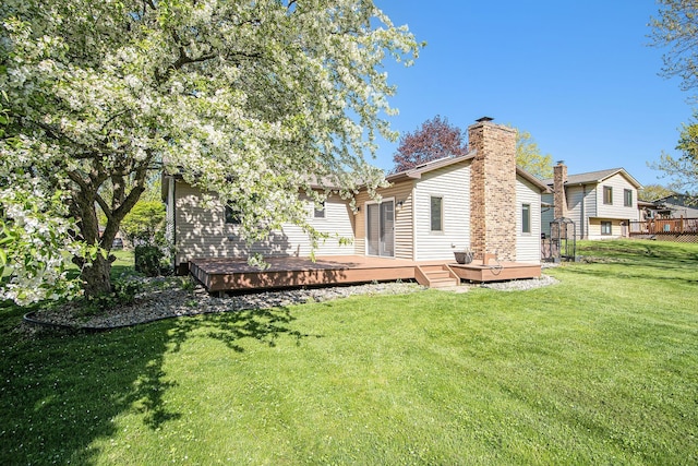 rear view of property with a deck, a lawn, and a chimney