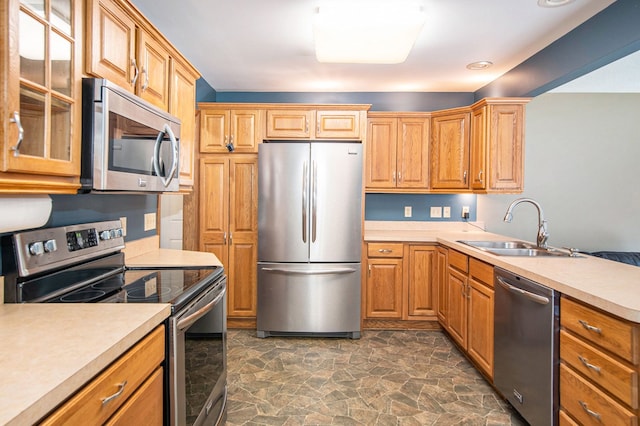 kitchen featuring appliances with stainless steel finishes, a sink, dark stone finish floors, light countertops, and glass insert cabinets