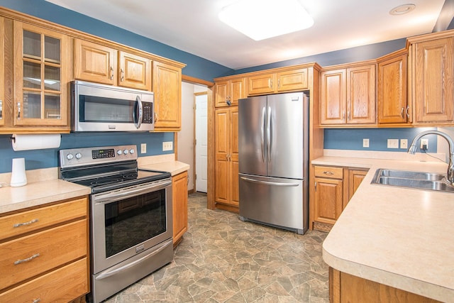 kitchen featuring appliances with stainless steel finishes, a sink, light countertops, glass insert cabinets, and stone finish floors
