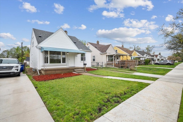bungalow-style home with roof with shingles, fence, a front yard, and concrete driveway