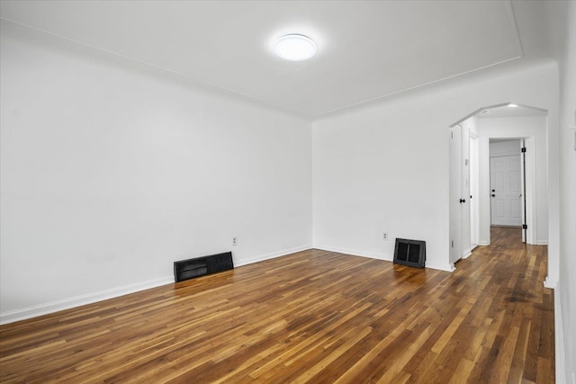 unfurnished room featuring arched walkways, baseboards, wood finished floors, and visible vents