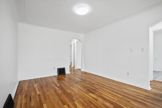 spare room featuring visible vents, arched walkways, baseboards, and wood finished floors