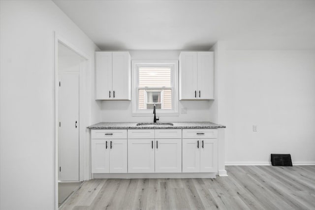 kitchen with white cabinetry, light stone countertops, a sink, and light wood-style floors
