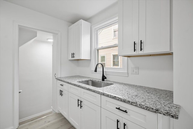 kitchen with light stone countertops, a sink, baseboards, light wood-style floors, and white cabinetry