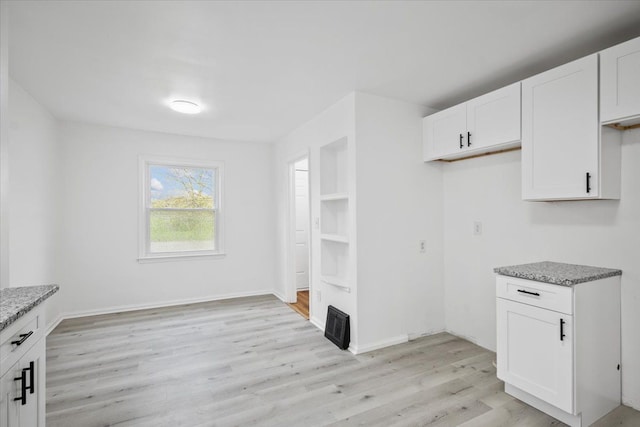 kitchen featuring light stone counters, white cabinets, baseboards, and light wood-type flooring