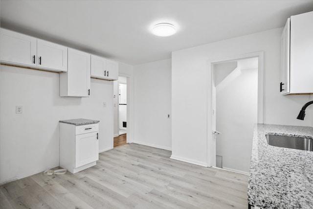 kitchen with white cabinetry, light stone counters, and a sink