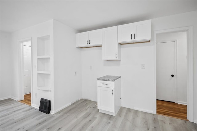 kitchen featuring baseboards, white cabinets, light stone countertops, and light wood-style flooring
