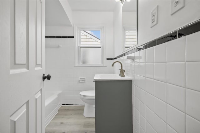 bathroom featuring vanity, toilet, a tub, tile walls, and wood finished floors