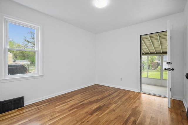 empty room featuring baseboards, a wealth of natural light, wood finished floors, and visible vents