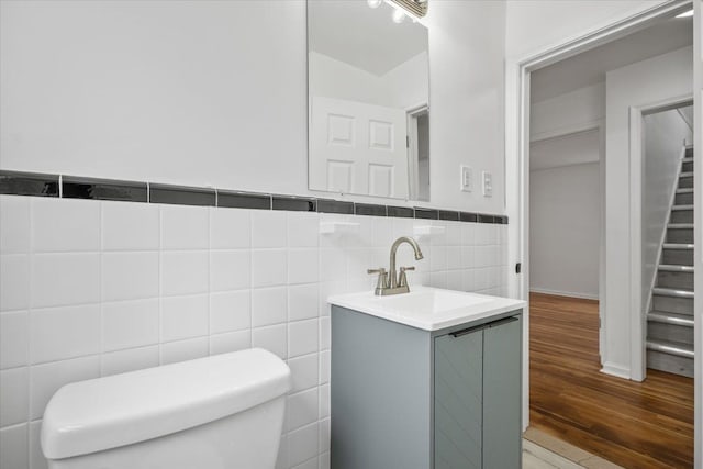 bathroom featuring tile walls, wood finished floors, a wainscoted wall, vanity, and toilet