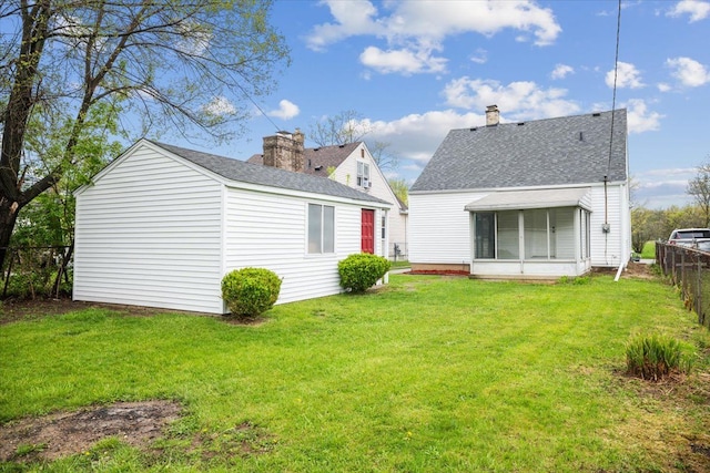 rear view of house featuring fence, a shingled roof, a yard, and a chimney
