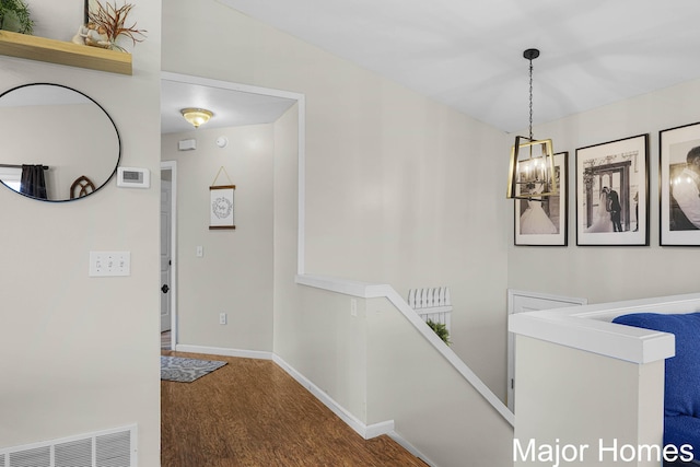 corridor with an inviting chandelier, baseboards, an upstairs landing, wood finished floors, and visible vents