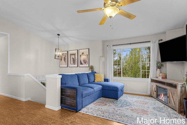 living area featuring baseboards, ceiling fan with notable chandelier, and wood finished floors