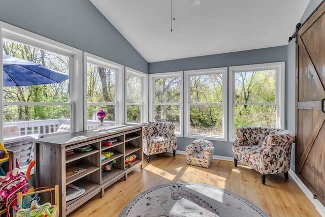 sunroom / solarium with plenty of natural light, a barn door, wood finished floors, and vaulted ceiling