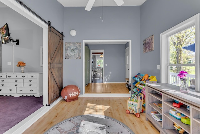 game room with a ceiling fan, baseboards, a barn door, and wood finished floors