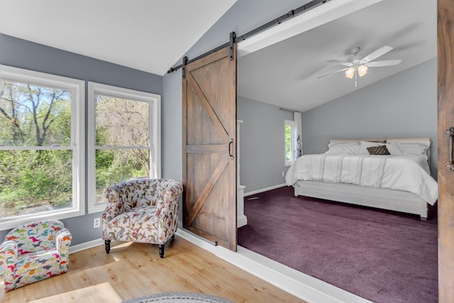 bedroom with baseboards, vaulted ceiling, a barn door, and wood finished floors