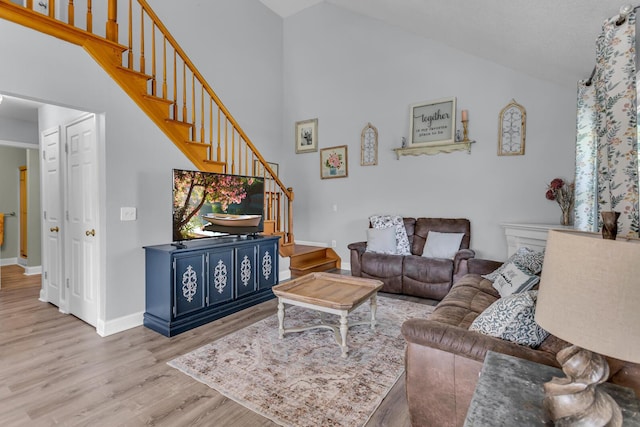 living area with baseboards, high vaulted ceiling, wood finished floors, and stairway
